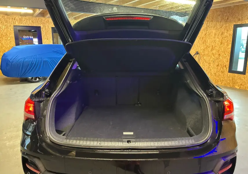 Vue arrière d'un Audi Q3 Sportback noir 2022 avec coffre ouvert, montrant l'espace de chargement vide en intérieur garage.