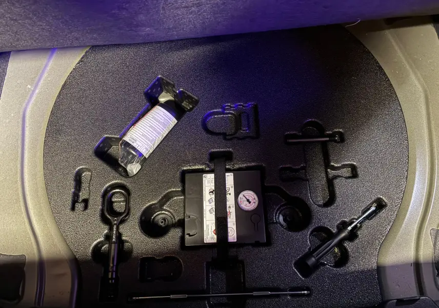 Vue plongeante sur le compartiment outils noir du coffre de l'Audi Q3 Sportback 2022 avec kit de réparation pneus.