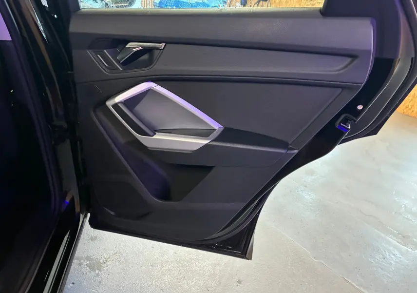 Vue rapprochée de la porte arrière gauche noire de l'Audi Q3 Sportback avec poignée argentée et panneau intérieur noir.