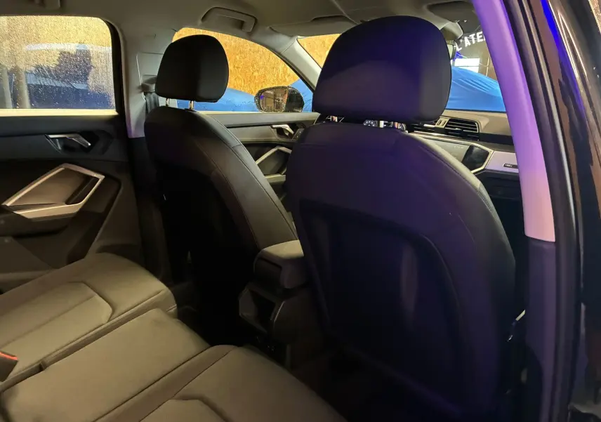 Vue intérieure arrière côté gauche de l'Audi Q3 Sportback noir, montrant les sièges en tissu et l'accoudoir central avant.