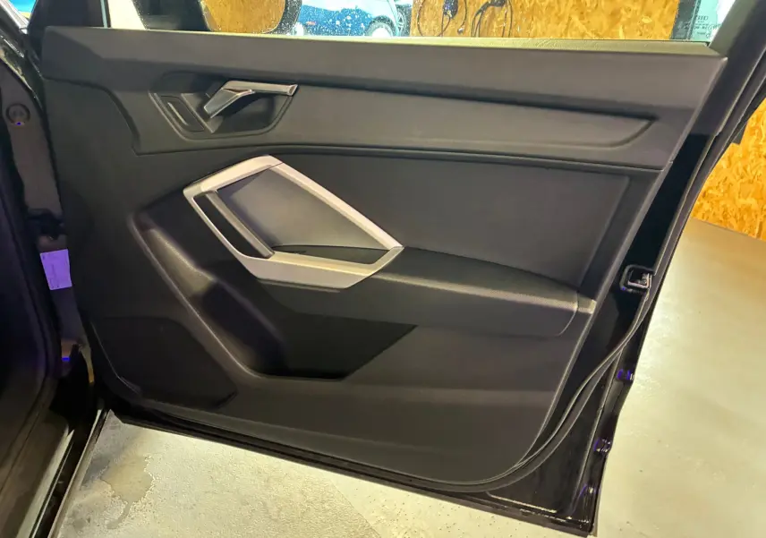 Vue rapprochée de la porte avant gauche noire de l'Audi Q3 Sportback 2022 avec poignée argentée et panneau intérieur noir.