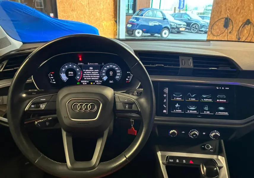 Vue intérieure centrée sur le volant cuir noir et l’écran tactile du tableau de bord de l’Audi Q3 Sportback 2022.