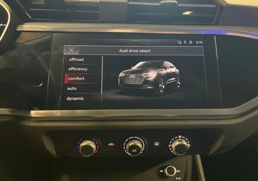 Écran tactile intérieur montrant un Audi Q3 Sportback noir en vue 3/4 avant avec menu de sélection de mode de conduite.