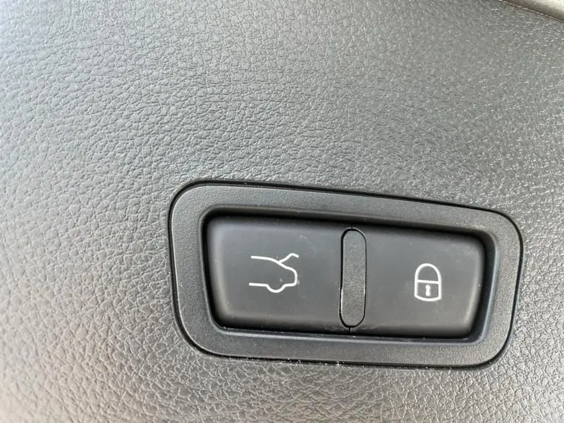 Boutons d'ouverture du coffre et de verrouillage dans l'habitacle d'une Alfa Romeo Tonale gris foncé, vue rapprochée.
