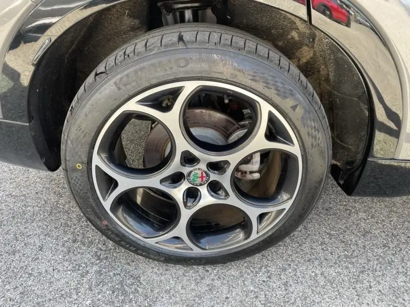 Gros plan sur la roue avant droite d'une Alfa Romeo Tonale gris foncé métal, avec jante distinctive à cinq cercles.