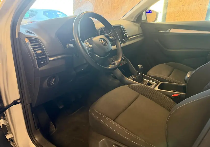 Intérieur du Skoda Karoq 2023 blanc, vue côté conducteur montrant le volant, tableau de bord et boîte manuelle.