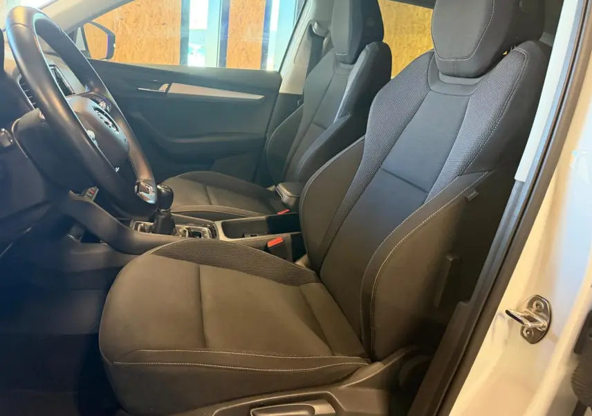 Vue intérieure côté conducteur du Skoda Karoq blanc 2023, mettant en valeur les sièges noirs et la boîte manuelle.