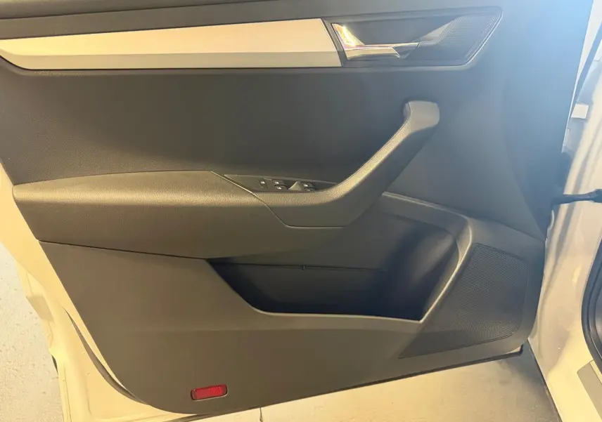 Intérieur côté gauche de la porte avant d'un Skoda Karoq blanc 2023, avec poignée et commandes de vitres visibles.