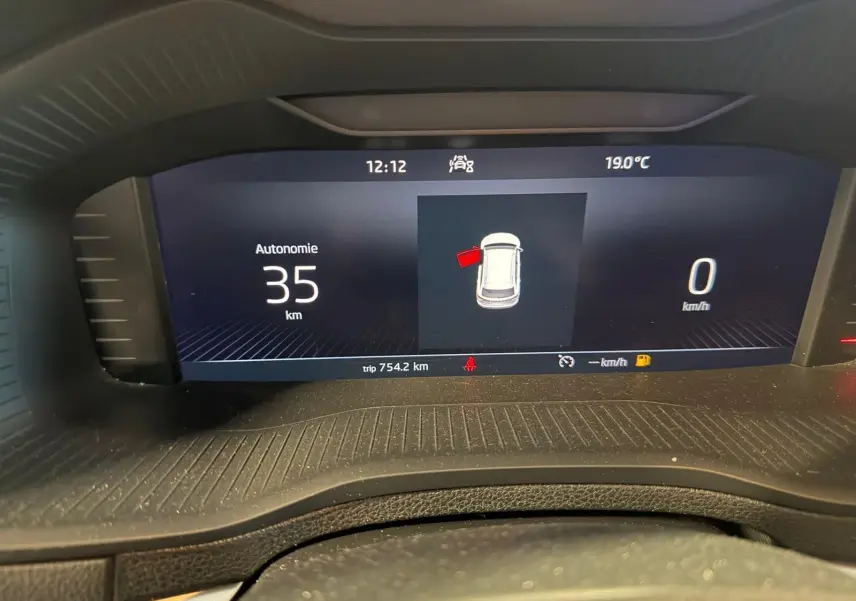 Affichage numérique du tableau de bord du Skoda Karoq blanc, montrant l'autonomie restante et la porte avant gauche ouverte.