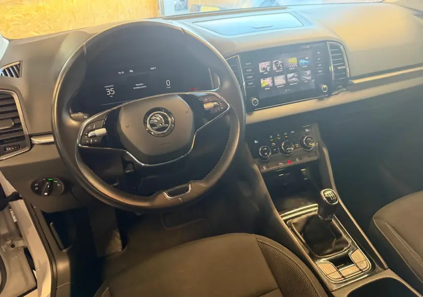 Vue intérieure du poste de conduite du Skoda Karoq blanc 2023, avec volant multifonction et boîte manuelle visible.