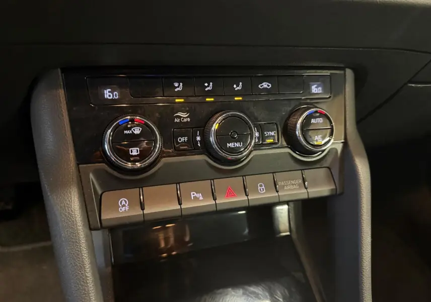 Gros plan sur la console centrale du Skoda Karoq blanc 2023, avec commandes de climatisation et boutons fonctionnels.