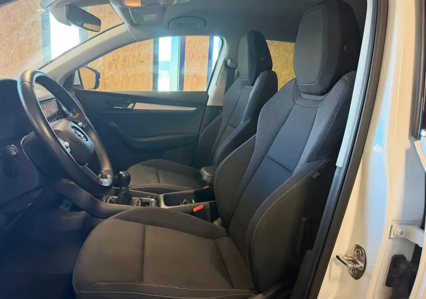 Intérieur du Skoda Karoq 1.5 TSI 2023 en blanc, vue côté conducteur montrant sièges noirs et volant avec boîte manuelle.