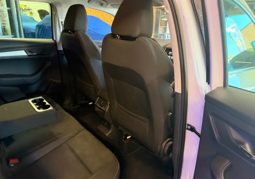 Vue intérieure arrière droite du Skoda Karoq blanc 2023, montrant les sièges noirs et la console centrale avec porte-gobelets.