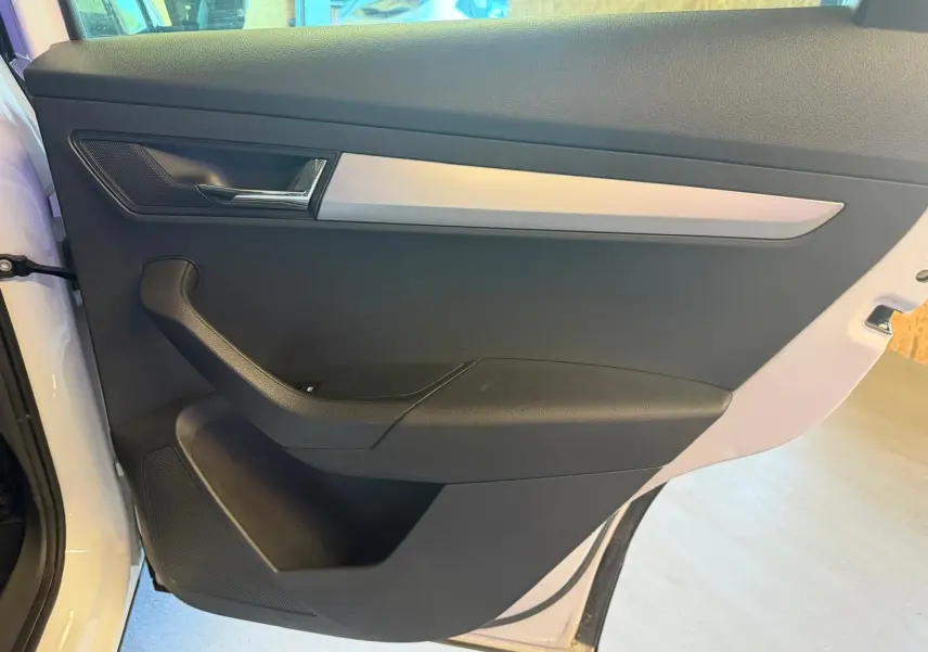 Vue intérieure de la porte avant gauche du Skoda Karoq blanc 2023, avec poignée noire et insert argenté.