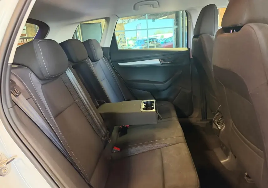 Vue intérieure côté gauche des sièges arrière noirs d'un Skoda Karoq blanc 2023 avec accoudoir central et porte-gobelets.