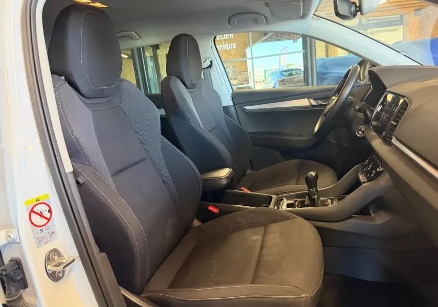 Vue intérieure côté conducteur du Skoda Karoq blanc 2023, montrant les sièges noirs et la boîte manuelle.