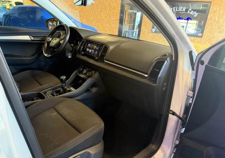 Intérieur avant droit du Skoda Karoq blanc 2023, montrant tableau de bord, volant et levier de vitesses manuel.