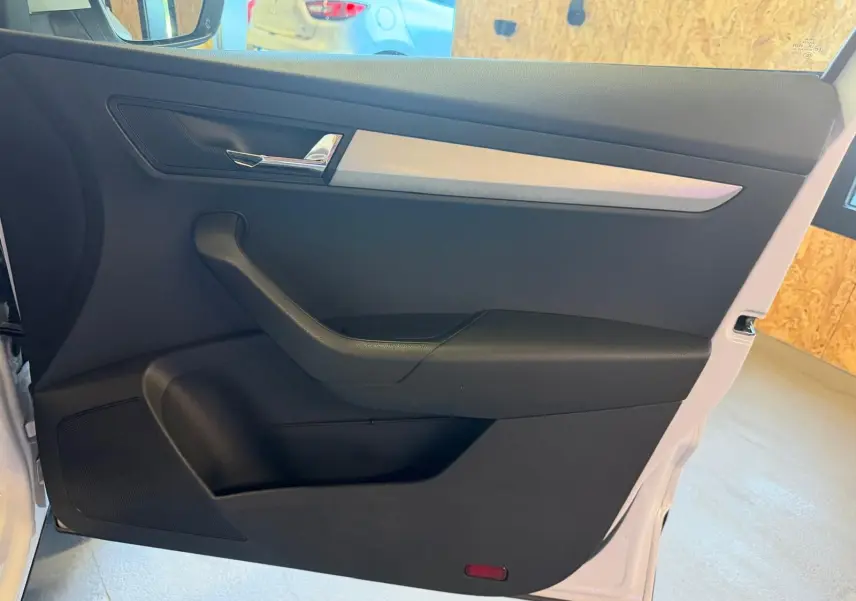 Vue intérieure de la porte avant gauche d’un Skoda Karoq blanc 2023, avec garniture noire et insert argenté.