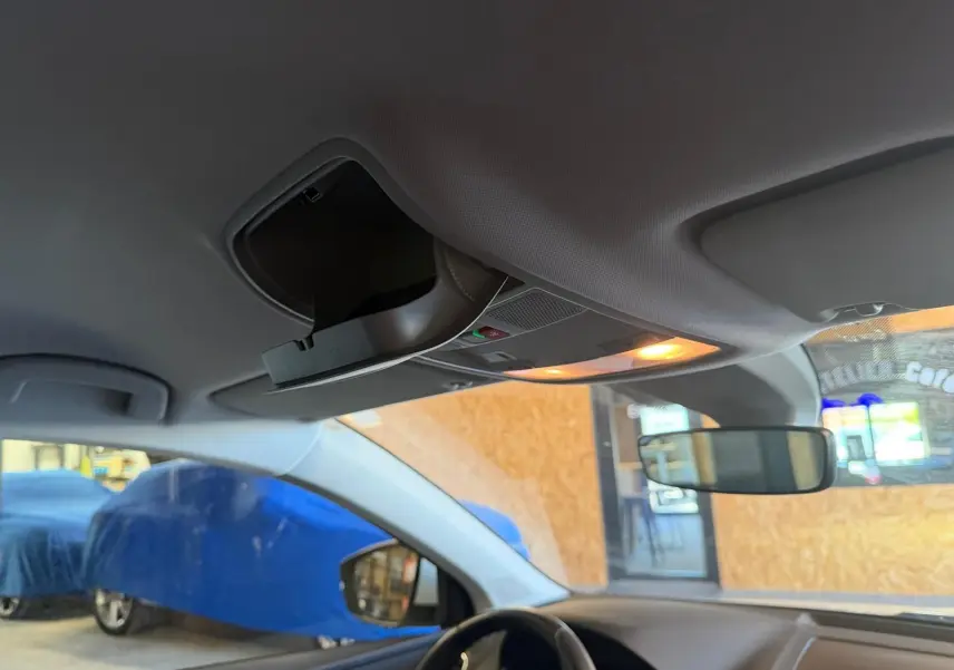 Vue intérieure du plafond avant du Skoda Karoq blanc 2023, montrant le rangement lunettes et l'éclairage intérieur allumé.