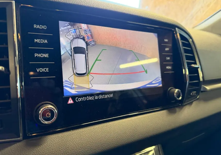 Écran central du Skoda Karoq blanc 2023 montrant la caméra de recul avec alertes de distance, vue intérieure côté droit.