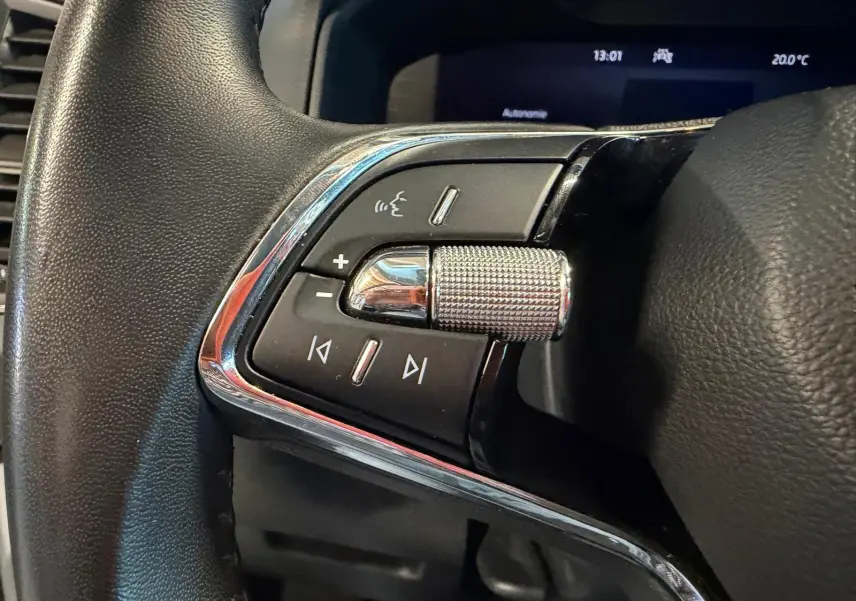 Gros plan sur les commandes gauche du volant du Skoda Karoq blanc 2023, avec molette et boutons multifonctions.