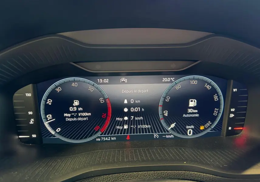 Tableau de bord numérique du Skoda Karoq blanc 2023, affichant vitesse, consommation et autonomie essence.