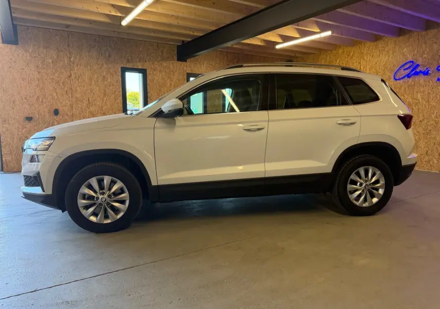 Vue de profil côté gauche d'un Skoda Karoq blanc 2023 avec jantes alliage, stationné en intérieur.
