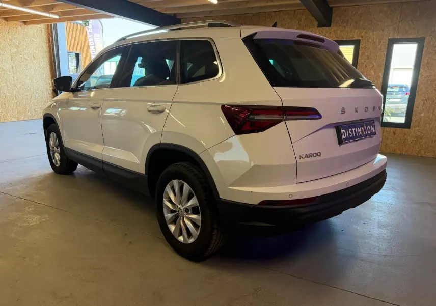 Vue 3/4 arrière droite d'un Skoda Karoq blanc 2023 avec jantes alliage et logo distinctif sur hayon.