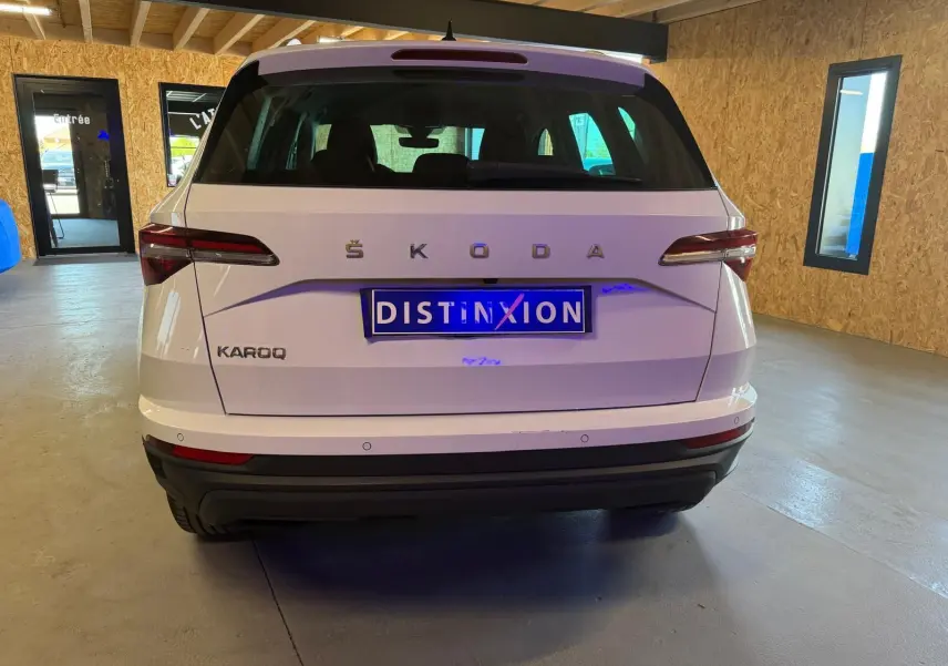 Vue arrière d'un Skoda Karoq blanc 2023 avec logo ŠKODA et plaque Distinxion dans un garage.