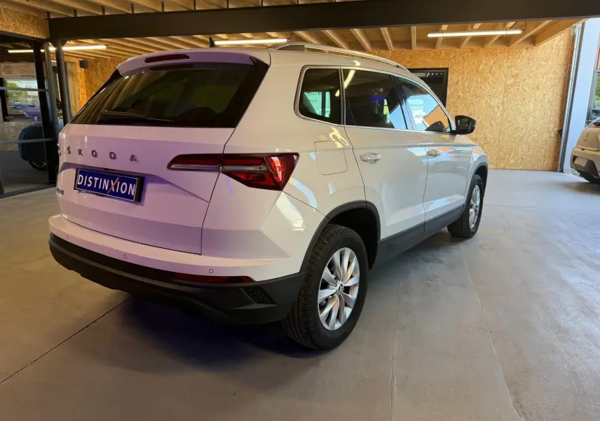 Vue 3/4 arrière droite d'un Skoda Karoq blanc 2023, avec feux arrière LED et jantes alliage, stationné en intérieur.