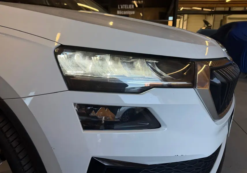 Gros plan sur l'avant gauche blanc du Skoda Karoq 1.5 TSI 150 Ambition 2023, mettant en valeur le phare et la calandre.