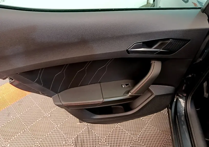 Vue rapprochée de la porte avant gauche d’une CUPRA Formentor gris foncé, avec surpiqûres rouges et poignée intégrée.