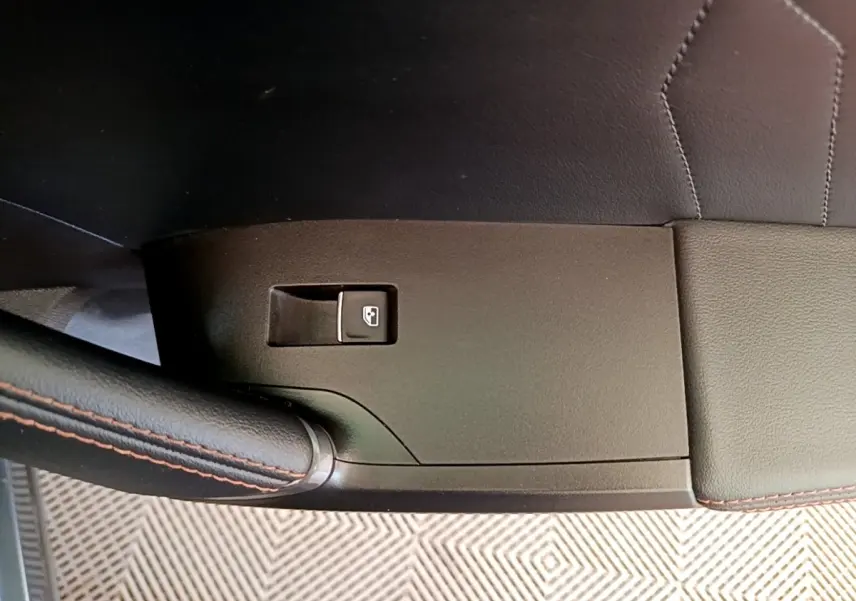 Gros plan sur la commande de lève-vitre côté conducteur avec surpiqûres orange sur cuir noir.