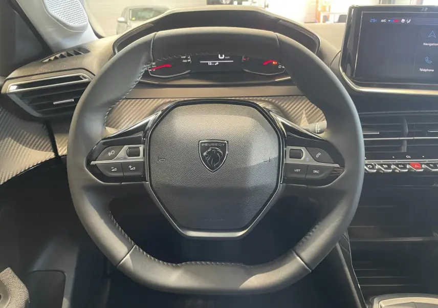 Vue intérieure centrée sur le volant cuir noir de la Peugeot 208 2025 avec tableau de bord et écran tactile.