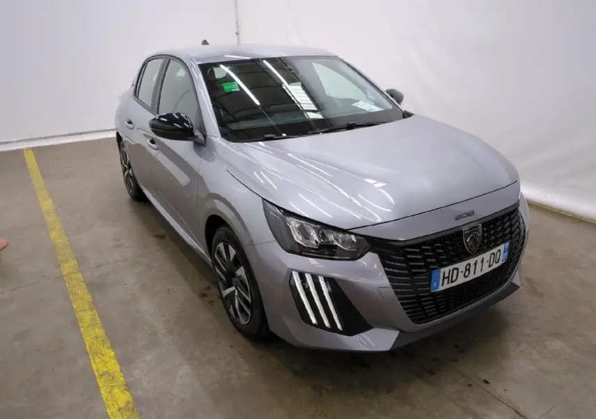 Peugeot 208 gris clair vue 3/4 avant droit avec calandre noire et feux LED signature 3 griffes.