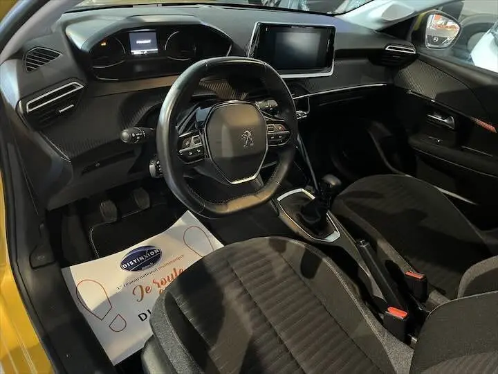 Vue intérieure côté conducteur de la Peugeot 208 jaune Faro Metal, avec tableau de bord moderne et volant multifonction.