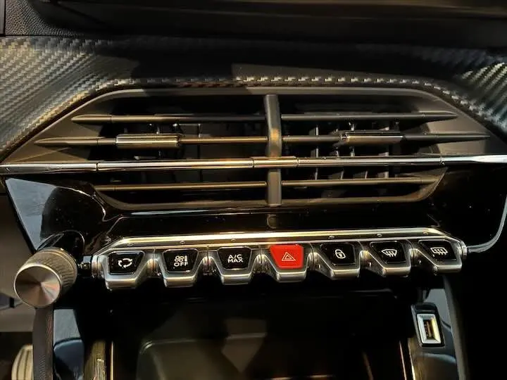 Gros plan sur la console centrale de la Peugeot 208 2020, mettant en valeur les boutons de commande et la finition noire brillante.