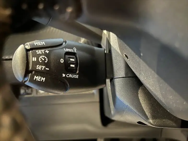 Gros plan sur la commande de régulateur de vitesse à gauche du volant d'une Peugeot 208 jaune Faro Metal de 2020.