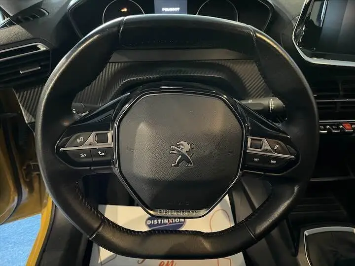Vue rapprochée du volant noir de la Peugeot 208 jaune Faro Metal, mettant en valeur les commandes intégrées.