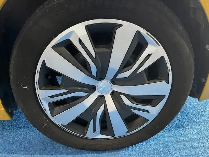 Gros plan sur la jante en alliage bicolore d'une Peugeot 208 jaune Faro Metal, montrant des traces d'usure sur le bord.