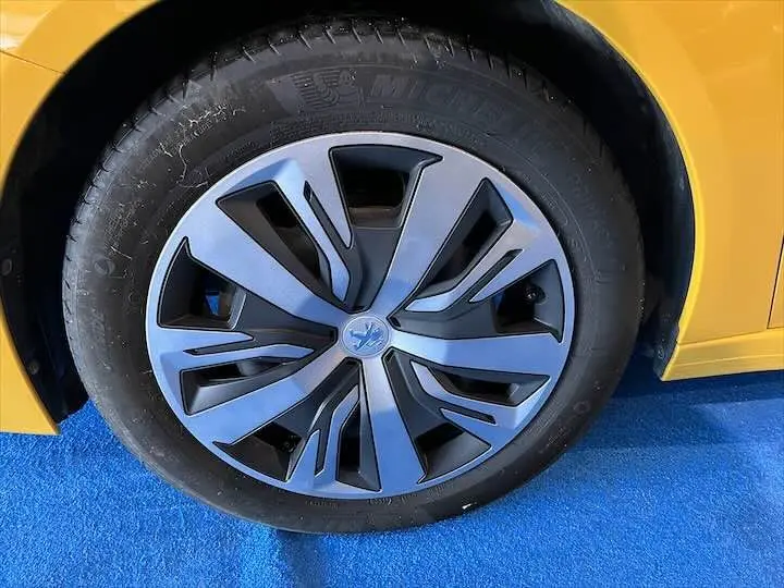 Gros plan sur la roue avant gauche d'une Peugeot 208 jaune Faro Metal, mettant en valeur la jante au design moderne.