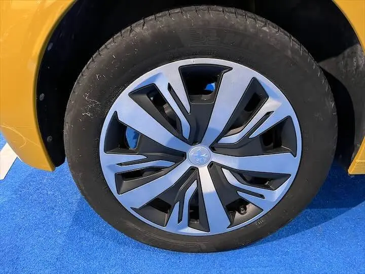 Gros plan sur la roue avant gauche d'une Peugeot 208 jaune Faro Metal, mettant en valeur la jante au design moderne.