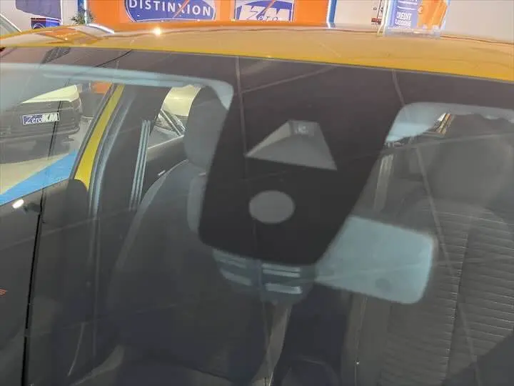 Vue intérieure par le pare-brise d'une Peugeot 208 jaune Faro Metal, montrant les sièges avant et le rétroviseur central.
