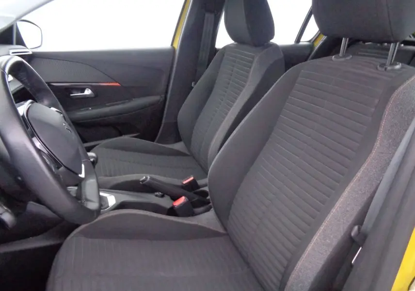 Vue intérieure côté conducteur de la Peugeot 208 jaune Faro Metal, sièges avant en tissu gris avec surpiqûres rouges.