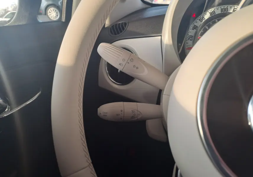 Détail des commandes de clignotants et régulateur sur le volant blanc d'une Fiat 500 essence hybride 2023.