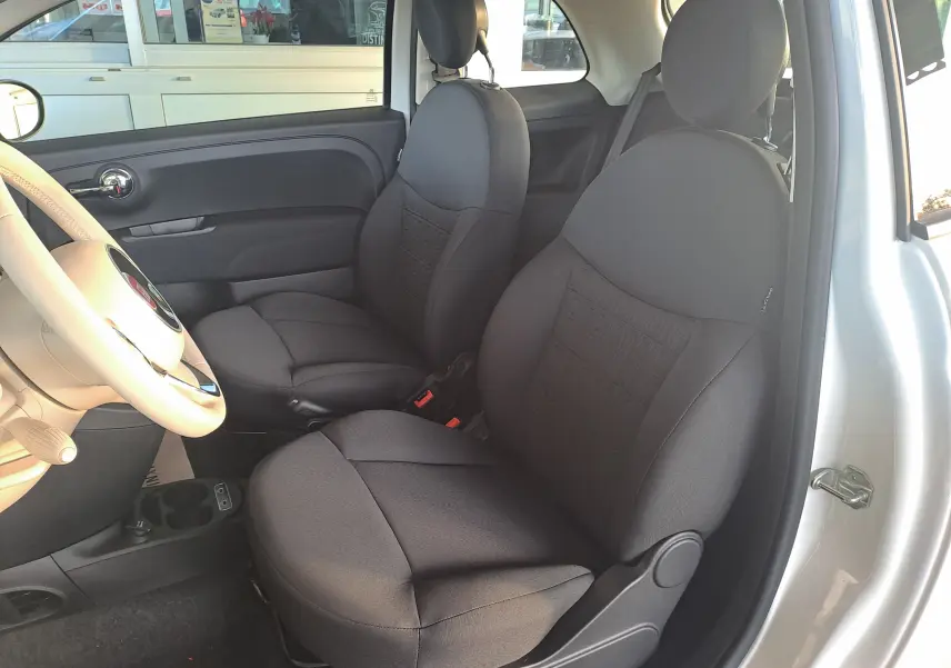 Vue intérieure côté gauche montrant les sièges noirs et le volant beige d'une FIAT 500 blanche 2023.