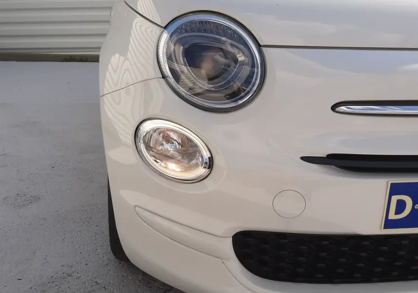 Gros plan sur l'avant gauche blanc d'une FIAT 500 2023, mettant en valeur ses phares ronds et la calandre noire.