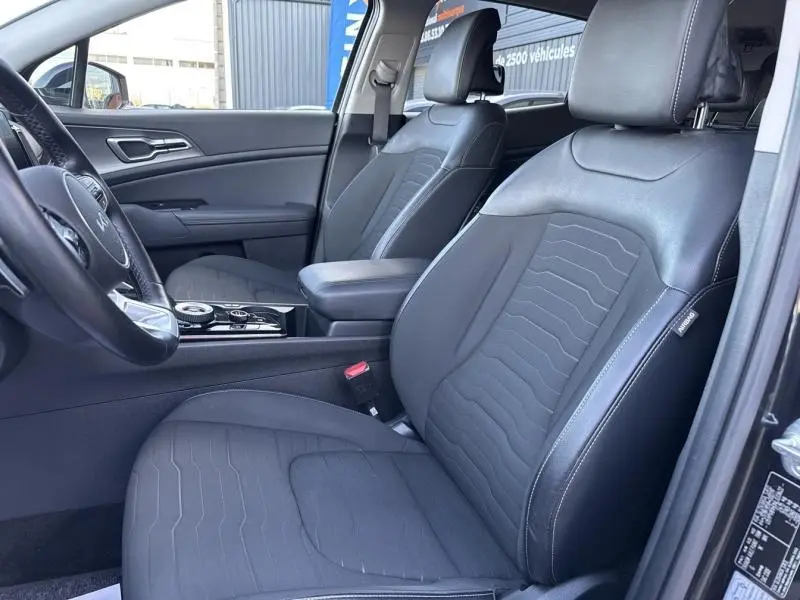 Vue intérieure côté conducteur du Kia Sportage 2022, sièges en cuir synthétique noir avec surpiqûres blanches et console centrale.