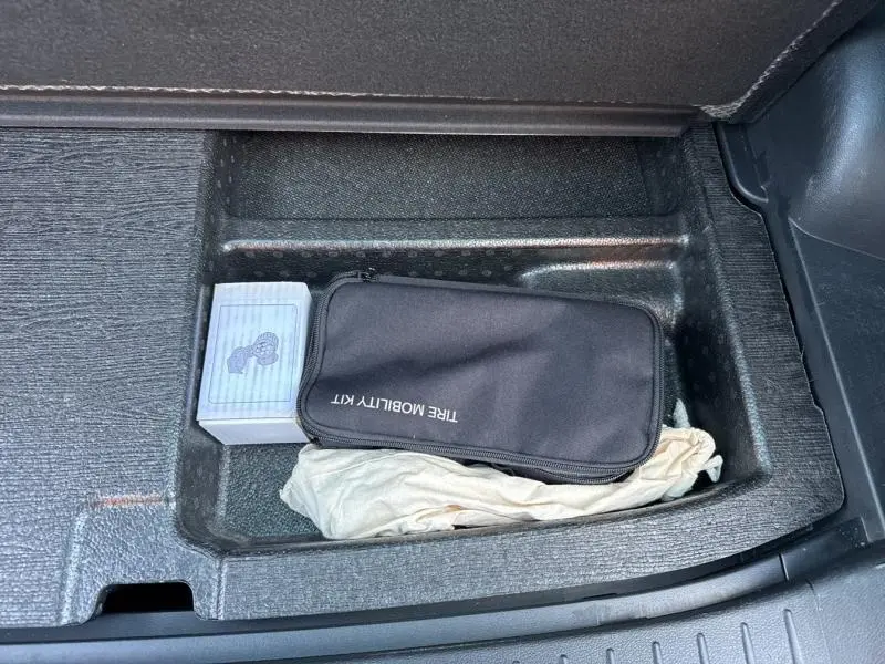 Rangement sous plancher de coffre du Kia Sportage noir, contenant un kit de mobilité pneu et une boîte grise.