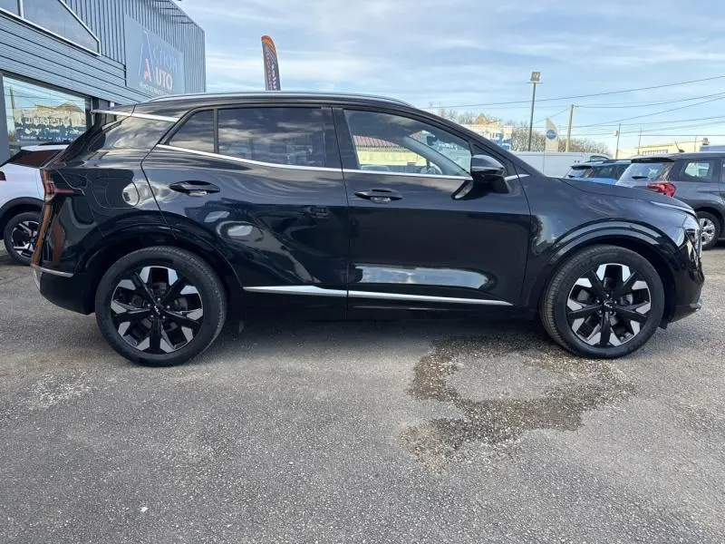Profil droit d'un KIA SPORTAGE noir Basalte métallisé 2022 avec jantes alliage noires et vitres teintées, stationné en extérieur.